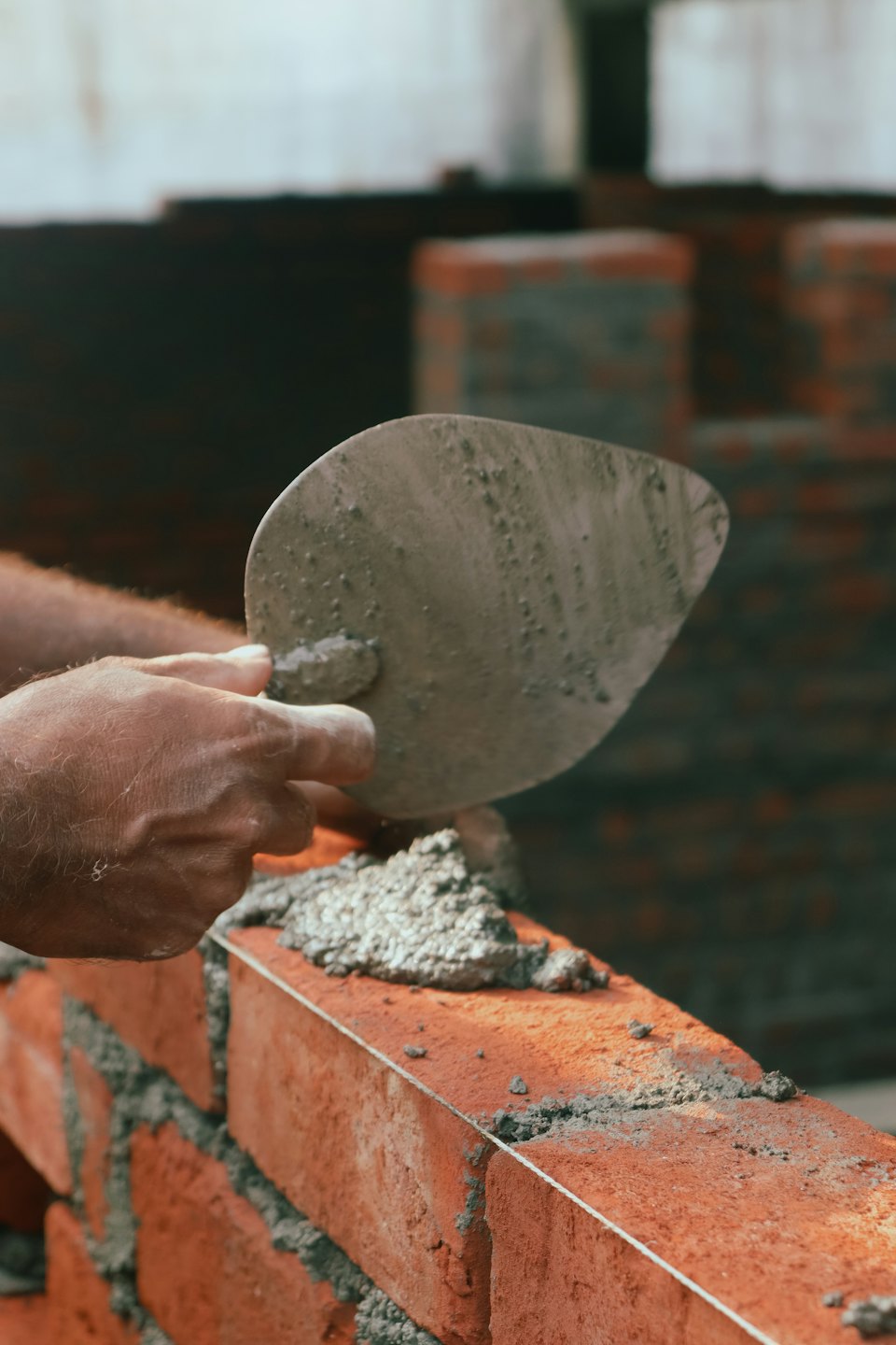 Hände tragen Mörtel auf rote Ziegel auf, um eine Mauer zu bauen.