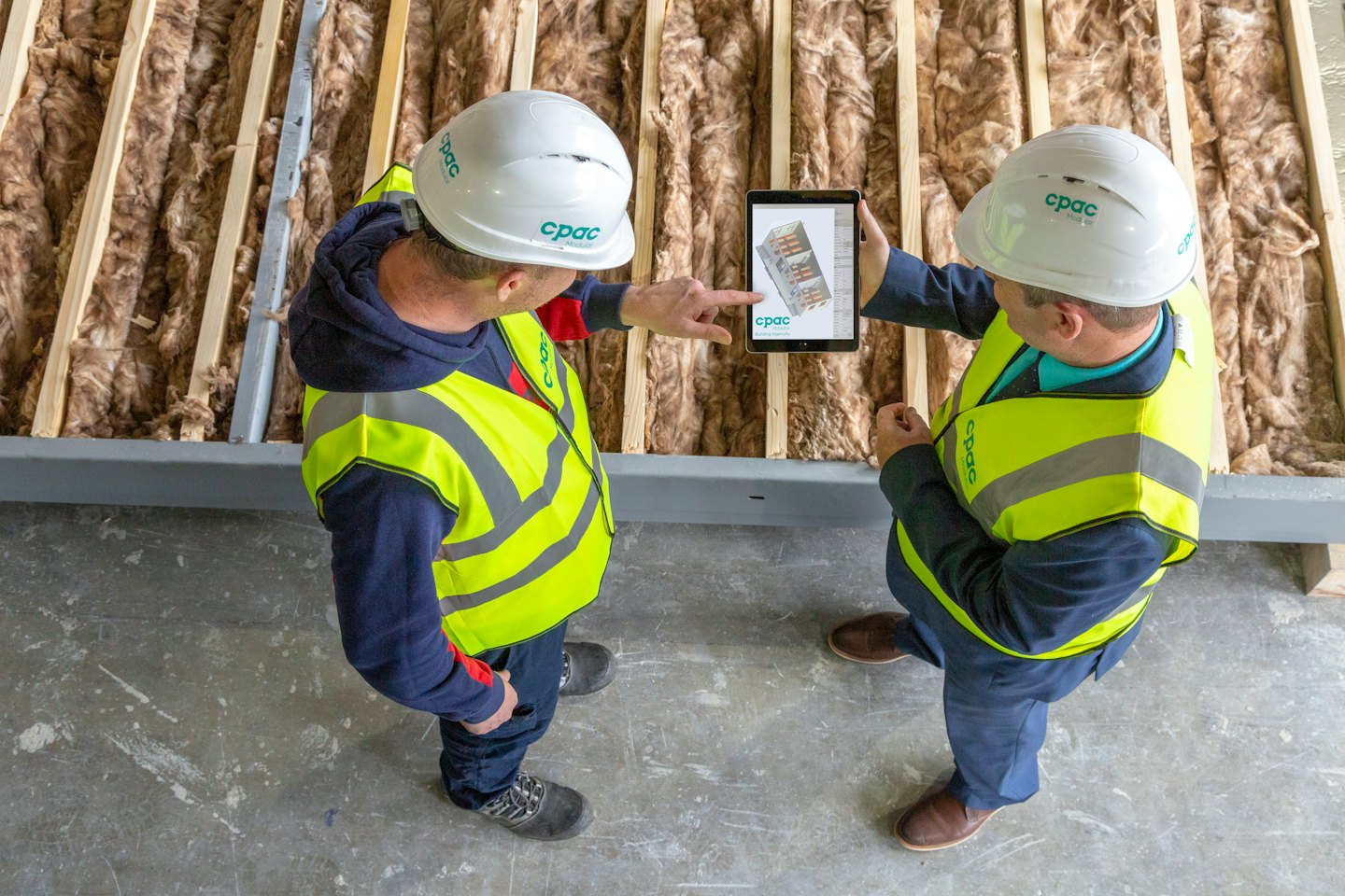 Zwei Bauarbeiter besprechen ein digitales Tablet auf einer Baustelle.